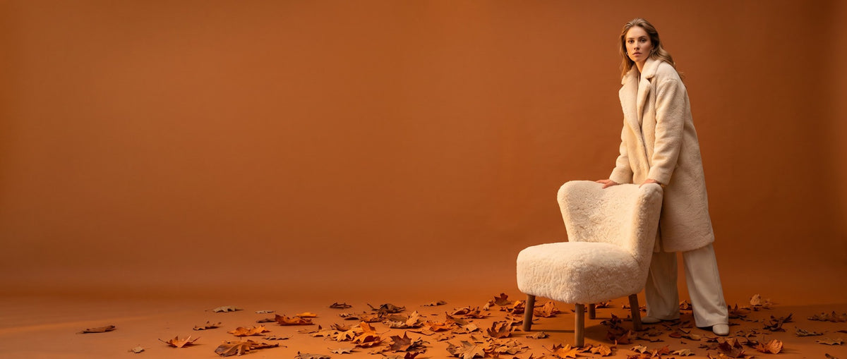 Woman in a sheepskin armchair by the wood burner, autumn forest outside the window